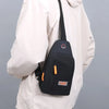 A black lightweight oxford cloth crossbody bag with an orange strap is shown against a light-colored jacket.