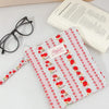 A pink and red floral plaid cotton tablet pouch with a secure closure resting on a white surface.