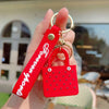 A red silicone heart beach bag keychain is held in a hand against a blurred outdoor background.
