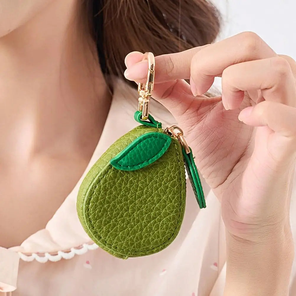 Eine Hand hält eine grüne, strukturierte Frucht-Charm-Münz-Geldbörsen-Schlüsselanhänger mit goldener Schnalle.