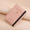 A pink leather passport holder with a black trim and a silver airplane logo resting on a light background.