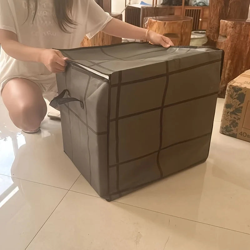 Une personne tient un sac de rangement pour vêtements pliable, gris foncé et robuste, à motif en grille sur un sol blanc bril