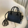 Sac à main en cuir PU noir minimaliste avec poignée supérieure sur une surface blanche.