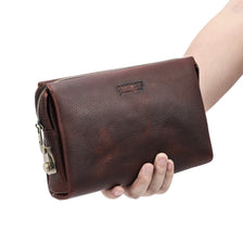 Portefeuille/clutch en cuir véritable marron pour homme tenu par une main.