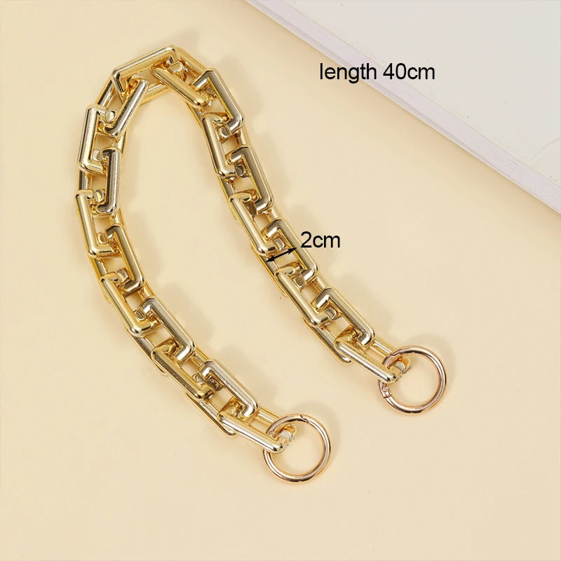 Correa de bolso de acrílico dorado, mide 40 cm con una sección de 2 cm, sobre fondo claro.