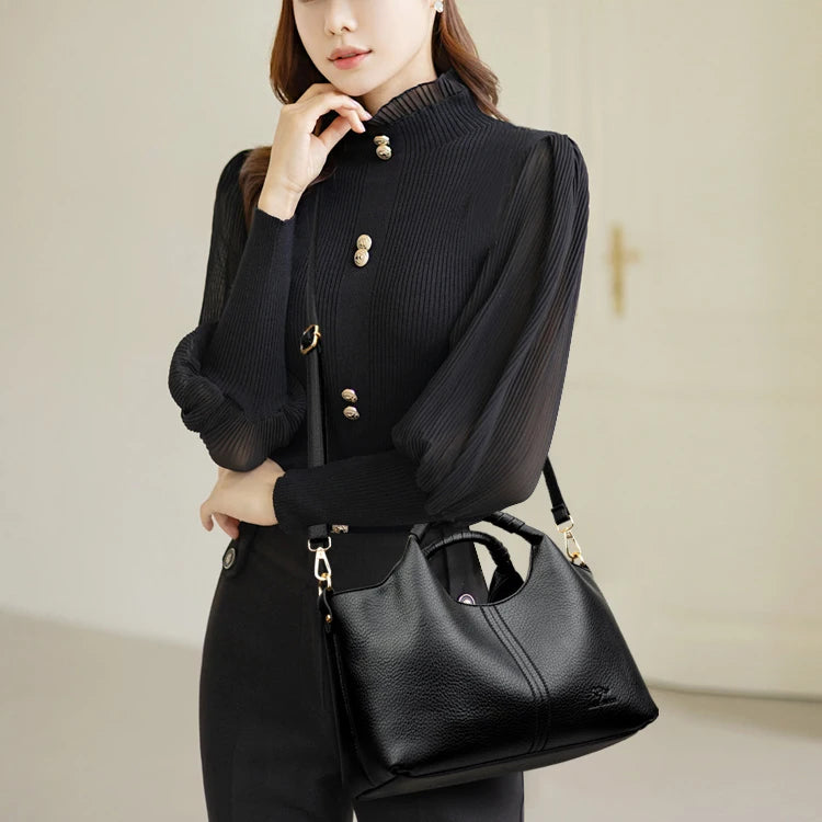 A woman wearing a black ribbed turtleneck top and trousers holds a black luxury soft leather tote bag.