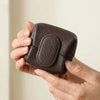 A hand holds a dark brown, leather-like coin purse with a snap closure.