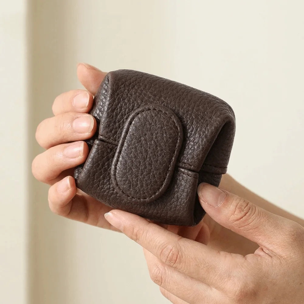 A hand holds a dark brown, leather-like coin purse with a snap closure.