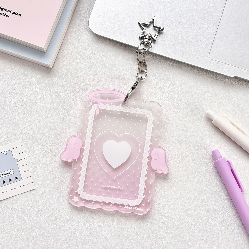 A clear pink acrylic photocard holder with a heart design and silver charm attached to a keyring.
