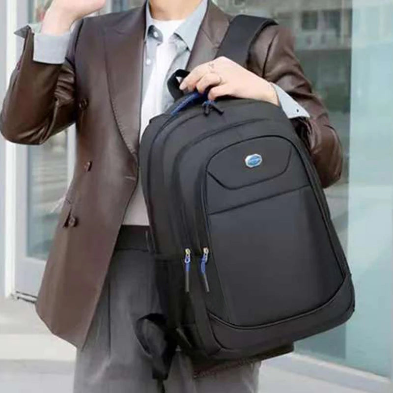 A person is carrying a black double-shoulder travel backpack while standing in a modern building setting.