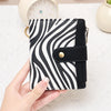 A hand holds a black and white striped compact wallet with a flap closure on a white surface.