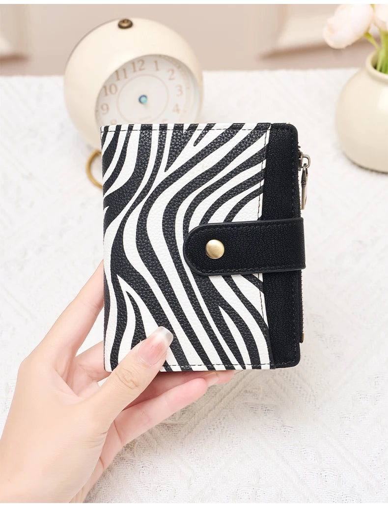 A hand holds a black and white striped compact wallet with a flap closure on a white surface.