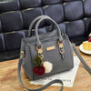 A gray vintage PU leather tassel handbag resting on a wooden surface.