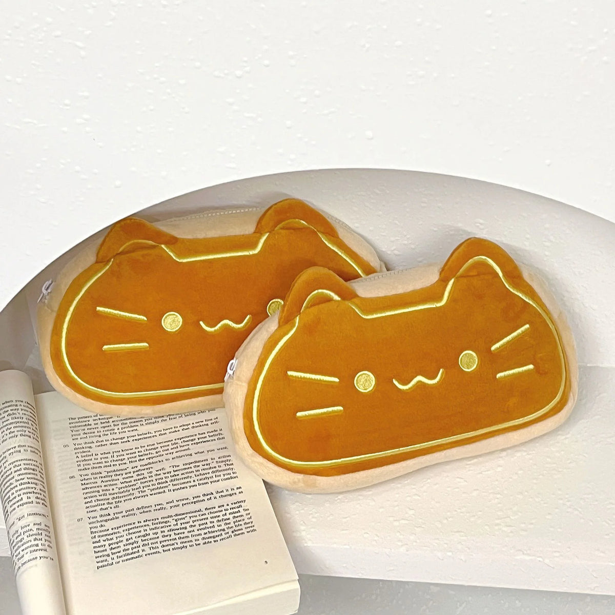 A soft orange caramel cat plush pencil pouch resting on a white surface.