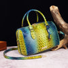 A luxury crocodile pattern crossbody tote bag in vibrant yellow and blue scales resting on a light surface next to a piece of