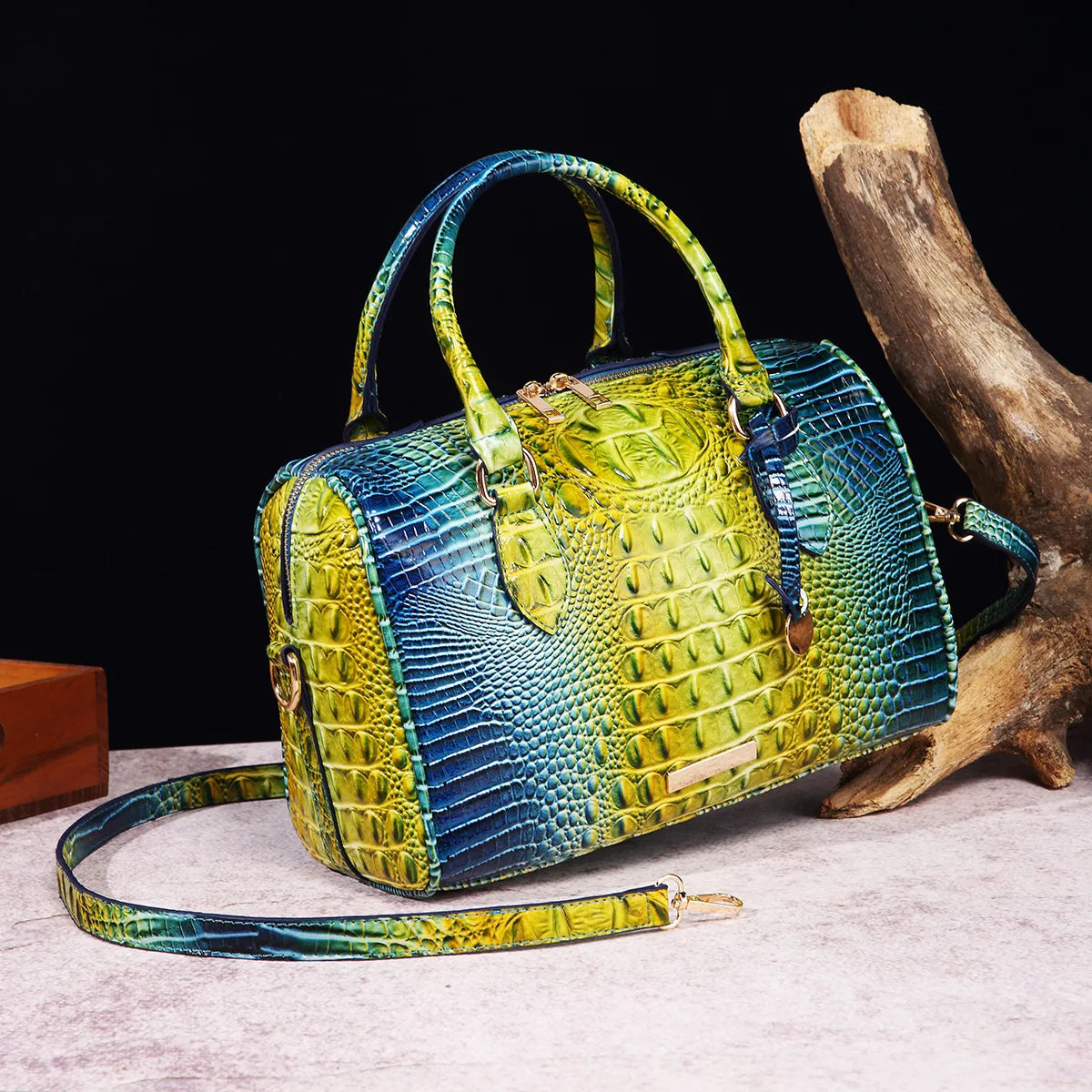 A luxury crocodile pattern crossbody tote bag in vibrant yellow and blue scales resting on a light surface next to a piece of