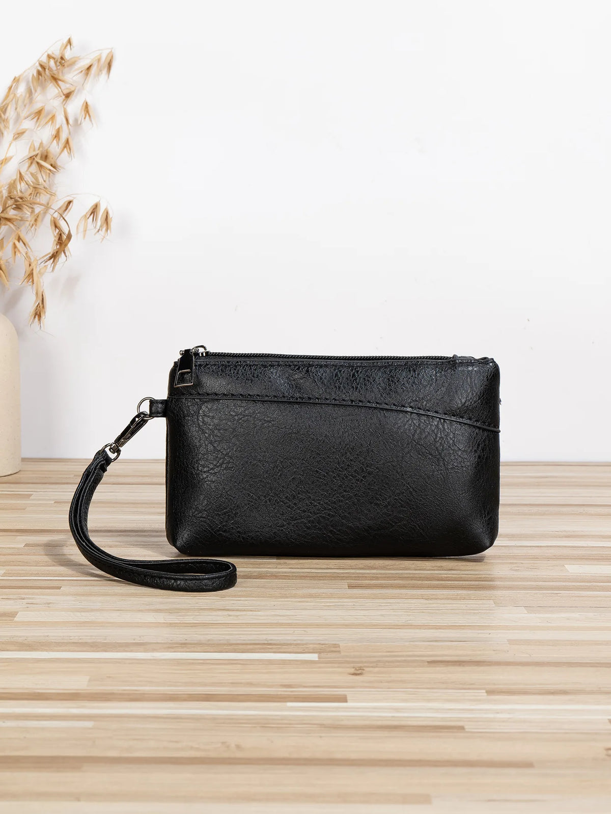 Black retro PU leather zipper wrist bag resting on a light wooden surface.