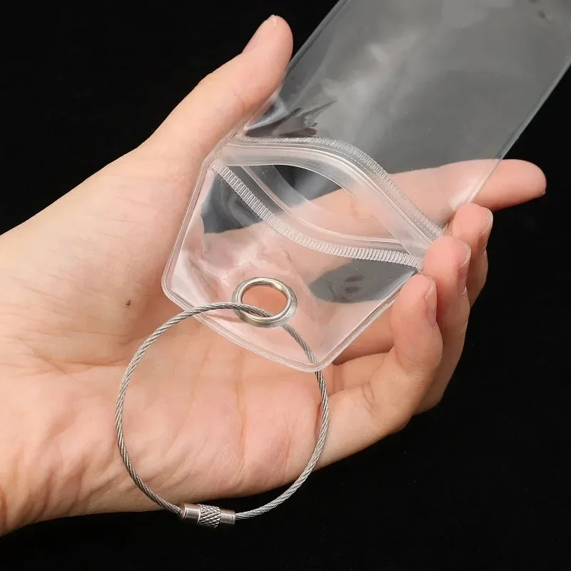 A hand holds a clear luggage tag with a steel ring attached, demonstrating the product.