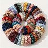 A circular arrangement of nineteen thin scrunchies hair ties in a variety of mixed pastel and deep jewel tones.
