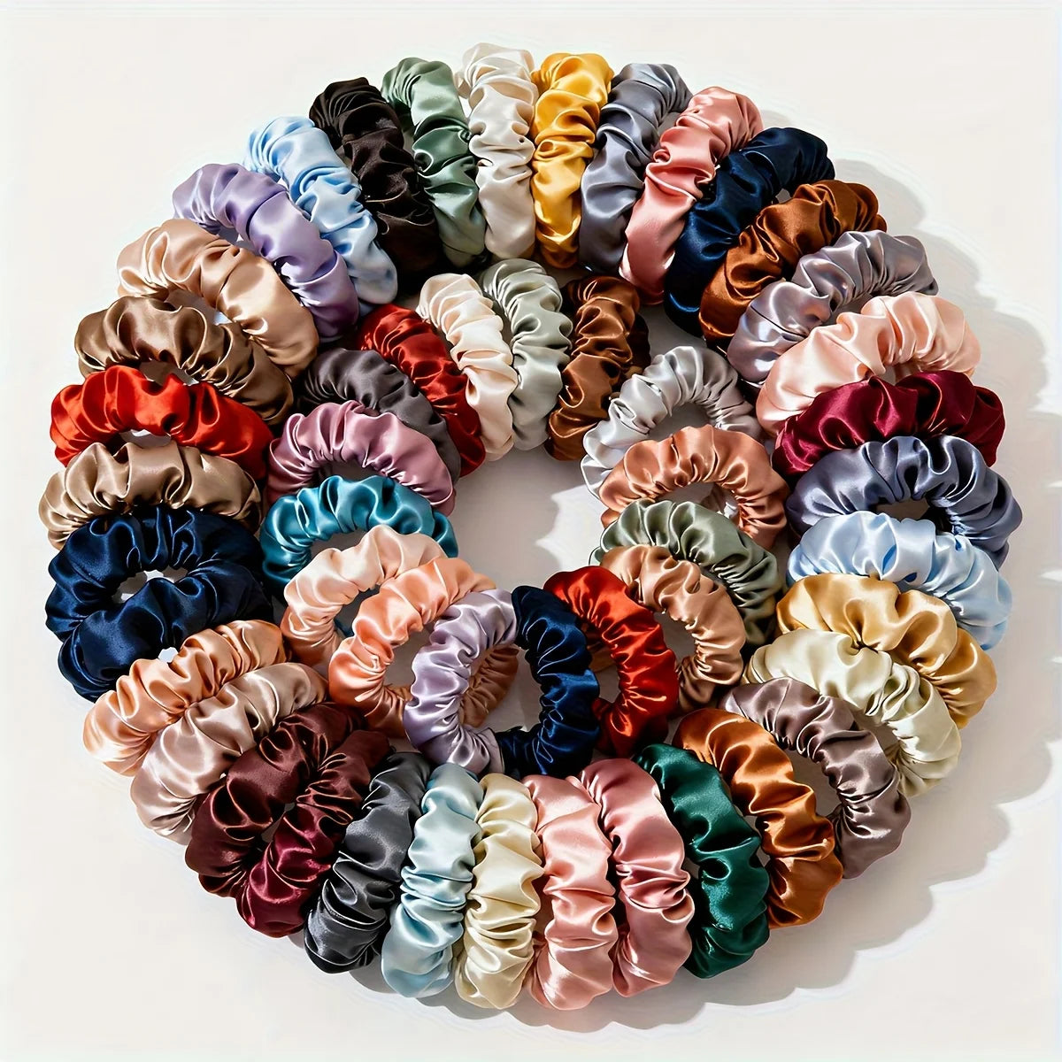 A circular arrangement of nineteen thin scrunchies hair ties in a variety of mixed pastel and deep jewel tones.