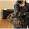A person is holding a leopard print canvas tote bag with an adjustable strap under a black leather coat.