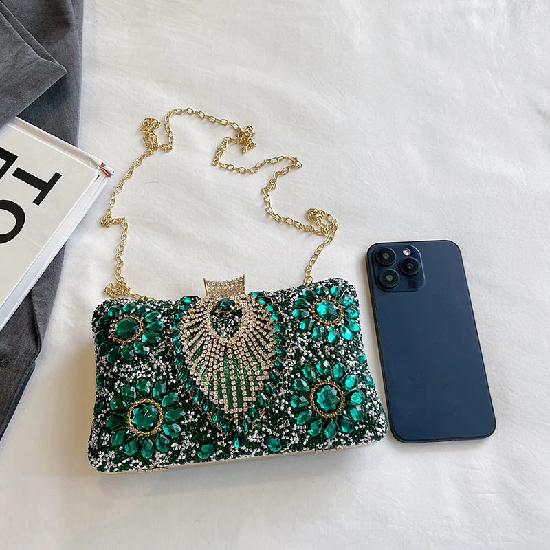 A sparkling green and gold rhinestone evening clutch bag resting on a white surface next to a smartphone.