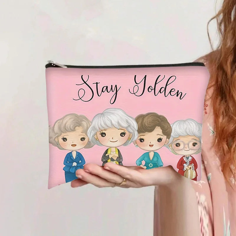 Bolsa de almacenamiento cosmético rosa con cremallera que dice 'Stay Golden' e ilustraciones de cuatro mujeres diversas.
