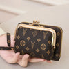 A dark brown fashion print accordion card holder wallet with gold-toned hardware and a black strap is held in a hand.