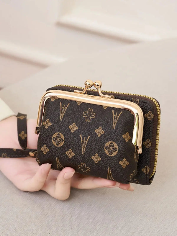A dark brown fashion print accordion card holder wallet with gold-toned hardware and a black strap is held in a hand.