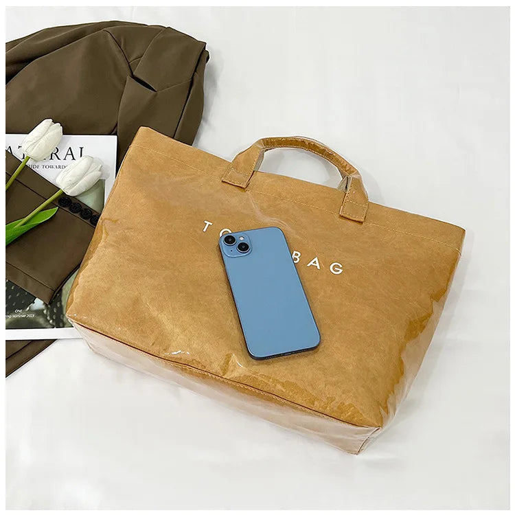 A light blue smartphone rests inside a brown transparent waterproof PVC tote bag next to a dark olive jacket.