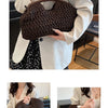 A close-up of a dark brown straw woven tote handbag being held by a woman in a white blazer.