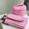 A pink striped Y2K makeup bag with a zipper and a fitted pouch is displayed on a white surface.