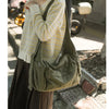 A woman wearing a yellow and white patterned sweater holds a large olive green cotton canvas shoulder crossbody bag.