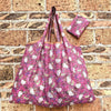 A pink and white patterned reusable shopping bag hanging against a brick wall.