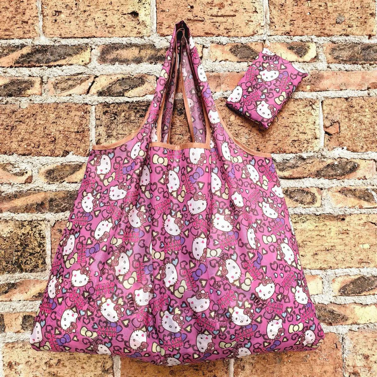 A pink and white patterned reusable shopping bag hanging against a brick wall.