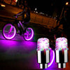 A pair of bright purple LED tire valve stem lights illuminating a bicycle wheel.
