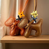 A tan PU leather puppy charm with a bow tie and yellow flower accents hanging from a brown leather strap.