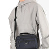 A man wearing a light gray waterproof jacket carrying a navy blue compact crossbody messenger bag.
