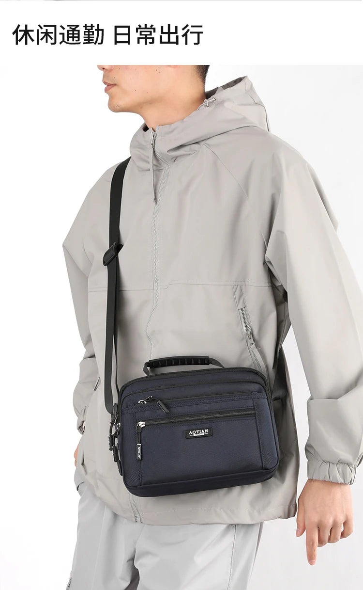 A man wearing a light gray waterproof jacket carrying a navy blue compact crossbody messenger bag.
