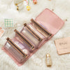 A pink portable detachable makeup bag with multiple zippered pouches rests on a fluffy white surface.