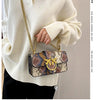 A person wearing a cream sweater holds an elegant retro crossbody bag with a patterned fabric and gold hardware.
