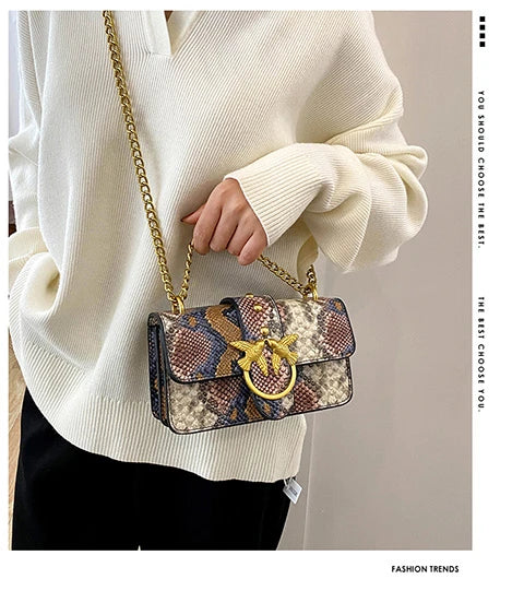 A person wearing a cream sweater holds an elegant retro crossbody bag with a patterned fabric and gold hardware.