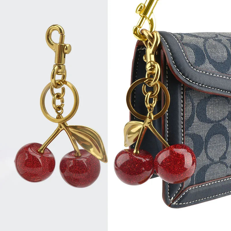 Gold-toned crystal apple charm keychain attached to a dark blue patterned bag.