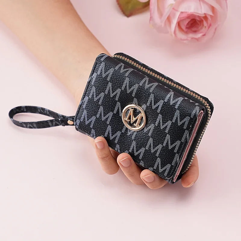 A black faux leather letter zipper wristlet wallet with a gold monogram and a zipper pull being held by a hand.