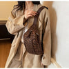 A woman is holding a brown leopard print crossbody bag with a dark strap under a beige trench coat.