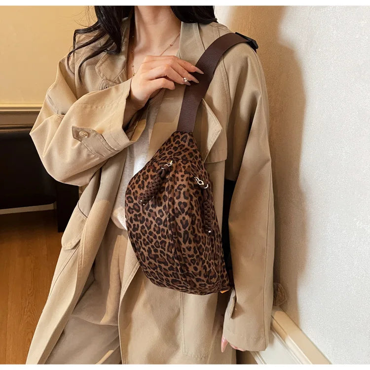 A woman is holding a brown leopard print crossbody bag with a dark strap under a beige trench coat.