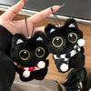 Colgante de llavero de peluche de gato negro sostenido por una mano contra un fondo desenfocado.