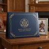 A dark blue elegant birth certificate holder with gold trim and an eagle emblem resting on a wooden surface.