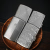 A silver metal cigarette case is shown open, resting on a wooden surface.