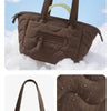A brown quilted tote bag with padded handles and a detachable strap shown against a cloudy background.